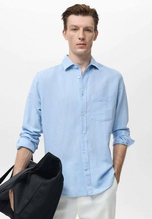 Helles blaues Hemd mit Knopfleiste aus weichem Stoff, ausgestattet mit einer Brusttasche und hochgekrempelten Ärmeln, kombiniert mit einer schwarzen Tasche.