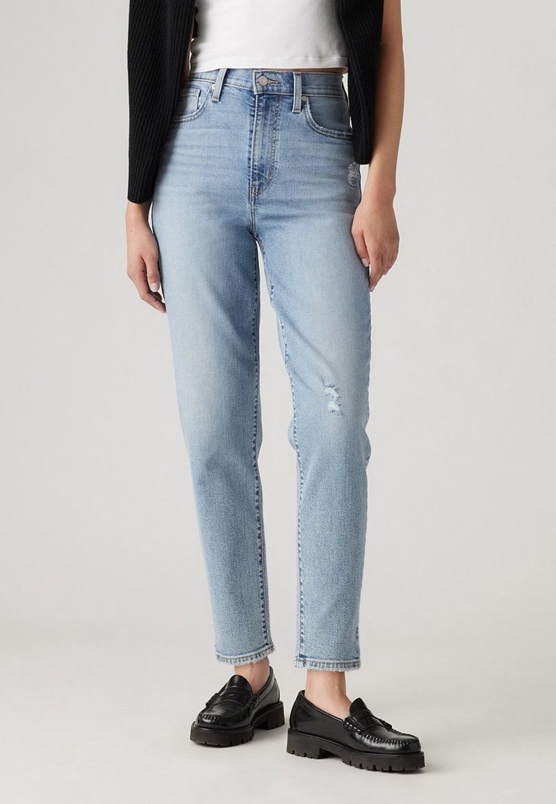 Hellblaue High-Waist-Jeans mit geradem Bein, leicht abgenutzten Details und fransigem Saum, kombiniert mit schwarzen Slippern.