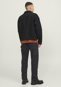 Zwarte denimjack met een klassiek ontwerp, gedragen over een roestkleurig shirt. Gepaard met zwarte cargobroek en zwarte laarzen.