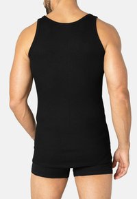 Black ribbed tank top with wide shoulder straps and a crew neckline, worn with matching black shorts, showcasing a fitted silhouette.