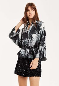Black and white patterned blouse with long, wide sleeves and a cinched waist, paired with a black sequined skirt.