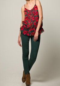 Röd blommönstrad topp med volangkant, matchad med gröna åtsittande byxor. Modellen bär bruna snörade ankelstövlar. Mjuk, lättviktig tyg.
