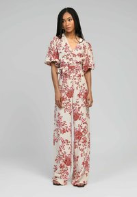 Combinaison florale crème avec des motifs de fleurs rouges et roses. Elle présente des manches courtes à volants, une taille cintrée et un design à jambes larges.
