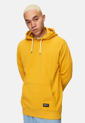 Yellow pullover hoodie with a front pocket, drawstrings, and a black "HONESTY" logo patch at the hem, made from soft cotton material.