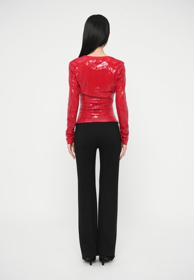 Punaste litritega pika varrukaga pluus, mis on kombineeritud mustade laiade pükstega. Pluus on keha järgiva lõike ja siledat tekstuuri.