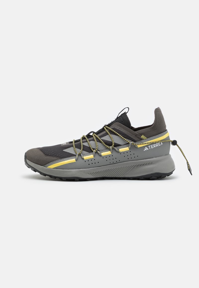 Scarpe da trail running con tomaia in rete grigia, accenti gialli e suola testurizzata. Dotate di lacci elastici e rinforzo nel tallone.