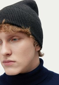 Svart ribbad stickad mössa med spetsig topp, bärs med en marinblå polokrage. Slät textur och åtsittande design, med mjukt och lätt material.