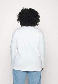 Vit långärmad skjorta med rundad halsringning och avslappnad passform. Tyget verkar mjukt, med raka sömmar och en något böjd nederkant.