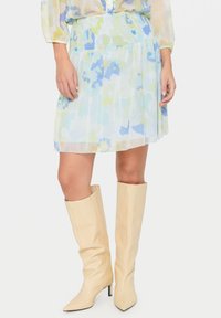 Vaaleansininen kukallinen hame, joka on valmistettu läpikuultavasta kankaasta ja jossa on rypytetty vyötärö. Yhdistetty vaaleanbeigeihin polveen saakka ulottuviin korkokenkiin.