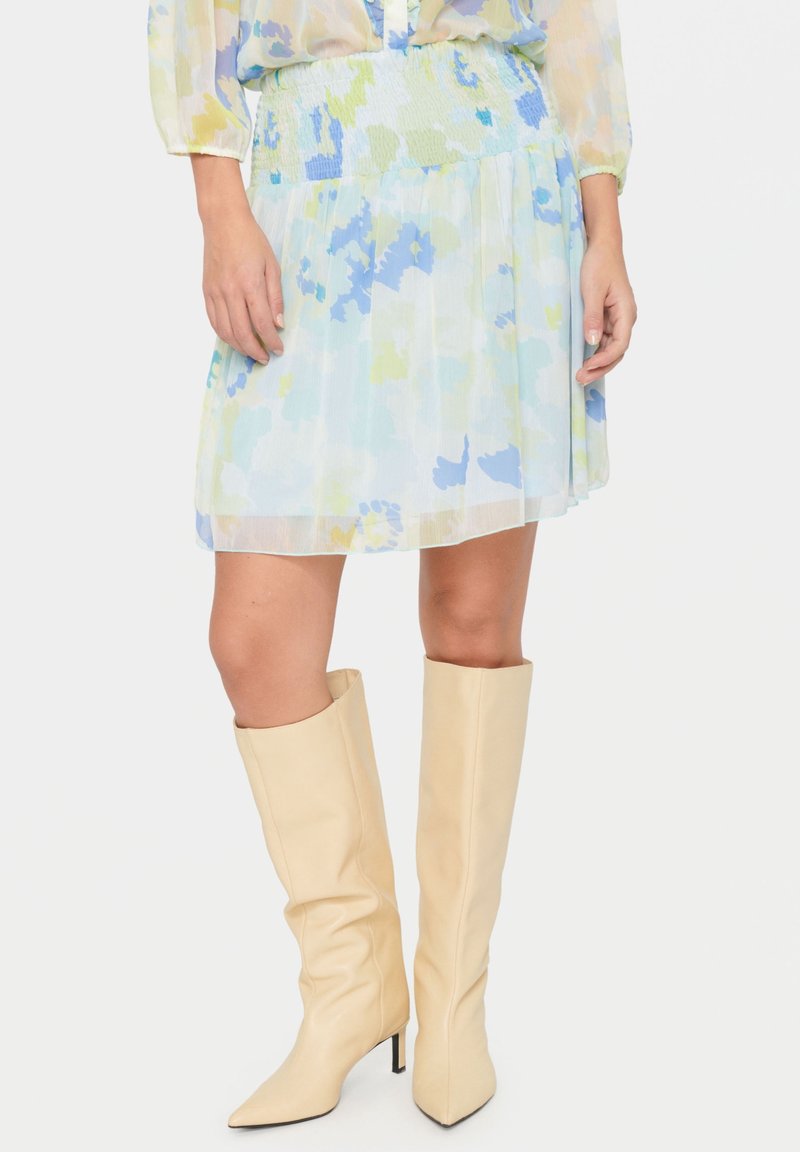 Vaaleansininen kukallinen hame, joka on valmistettu läpikuultavasta kankaasta ja jossa on rypytetty vyötärö. Yhdistetty vaaleanbeigeihin polveen saakka ulottuviin korkokenkiin.