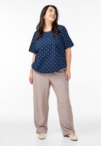 Top corto a maniche corte a pois blu navy abbinato a pantaloni in lino marrone chiaro. Il top presenta una vestibilità ampia e scollatura a girocollo; le scarpe sono ballerine beige.