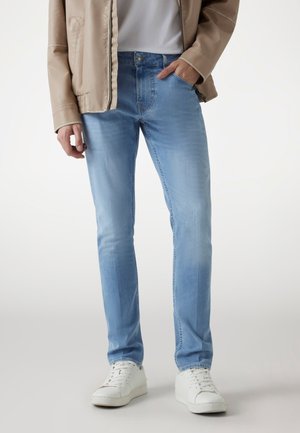 Hellblaue Jeans aus Denim mit schmaler Passform, die eine dezente Ausbleichung, ein Fünf-Taschen-Design und einen silbernen Knopfverschluss aufweisen. Getragen mit einem weißen T-Shirt und Turnschuhen.