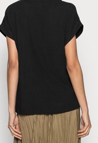 Svart linnetopp med korta ärmar och avslappnad passform. Har uppvikta ärmar och rak nederkant, kompletterad av en veckad beige kjol.