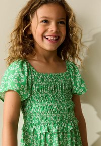 Zöld ruha fehér virágmintával, fodros ujjakkal és gumírozott felsőrésszel, fodros szegéllyel, könnyű anyagból.