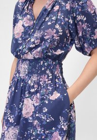 Blumenkleid aus marineblauem Stoff mit rosa und violetten Blumen, kurzen Puffärmeln, einem gerafften Taillenbund und Seitentaschen.