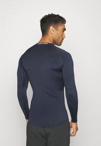 Marineblaues Langarm-Sportshirt mit schmalem Schnitt. Hergestellt aus glattem, elastischem Stoff. Mit "NIKE PRO"-Markierung am Nacken des Rückens.