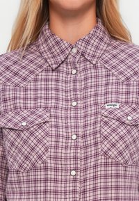 Chemise à carreaux violette à boutons en tissu texturé, dotée d'un col pointu, de deux poches poitrine et d'un label de logo sur la poche gauche.