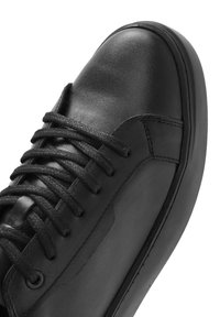 Baskets noires en cuir, avec un bout arrondi, des lacets plats, une surface texturée et une semelle en caoutchouc contrastante avec un détail de couture subtil.