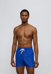 Μπλε μαγιό σορτς με λευκό κορδόνι, που δια θέτει μικρό λογότυπο. Κατασκευασμένο από λείο ύφασμα, σχεδιασμένο σε μήκος μέχρι τη μέση του μηρού.