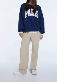 Granatowy, oversize'owy sweter z napisem "PARIS", beżowe spodnie szerokie w nogawkach i białe sneakersy. Widoczny kołnierzyk w pasiasty wzór pod spodem.