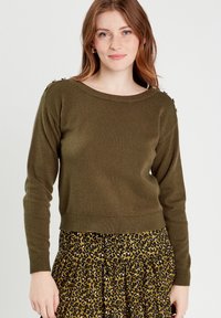 Olive green sweater with a wide neckline and long sleeves, featuring decorative buttons on the shoulder, paired with a leopard print skirt.