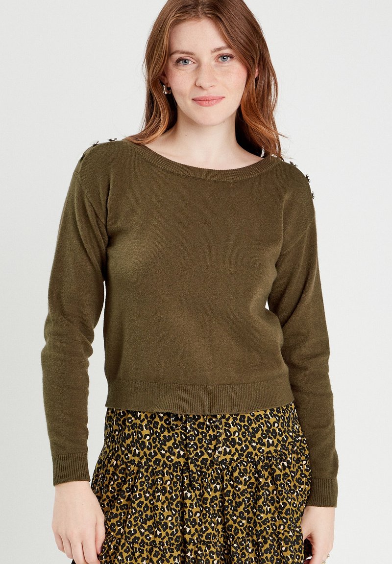 Olive green sweater with a wide neckline and long sleeves, featuring decorative buttons on the shoulder, paired with a leopard print skirt.