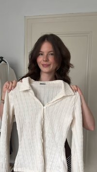 Camisa de manga longa bege clara com colarinho, de superfície texturizada e fecho por botões. Apresenta um corte relaxado e um padrão de rugosidade subtil.