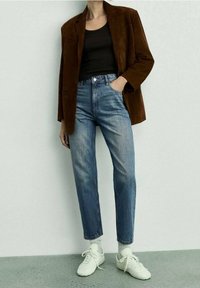 Blazer in suede marrone su una canotta nera a coste, abbinato a jeans chiari a vita alta e sneaker bianche.