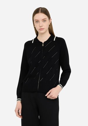 Maglione nero con cerniera, maniche lunghe, con accenti a strisce bianche e motivo testurizzato. Polsini e orlo a costine per un dettaglio aggiuntivo.