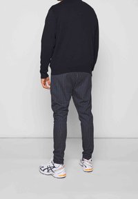 Czarna bluza, pasiaste szare i granatowe spodnie oraz białe trampki z pomarańczowymi akcentami. Widoczny widok z tyłu, styl casual streetwear.