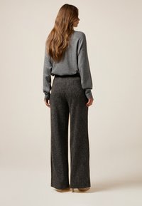 Grau gestrickter Pullover kombiniert mit weit geschnittenen, strukturierten, dunkelgrauen Hosen. Beide Kleidungsstücke haben einen entspannten Schnitt und dezente Muster.