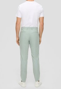 Svěže zelené kalhoty s texturovaným povrchem a slim fit střihem, obsahující dvě zadní kapsy a plochý pás, doplněné bílým tričkem.
