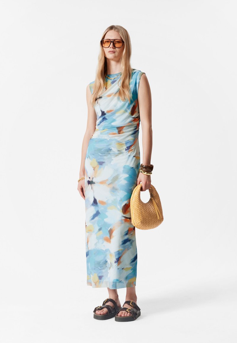 Maxikleid im abstrakten hellblauen Muster mit Spritzern von Orange und Gelb. Glattes Material, ärmelloses Design. Geflochtene Strohtasche, schwarze Sandalen.