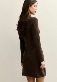 Brązowa dzianinowa sukienka z długimi rękawami, miękką fakturą i dopasowanym krojem, który lekko rozszerza się ku dołowi. Minimalistyczny design i neutralny kolor.