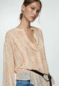 Lichte, doorschijnende blouse met een bloemprint in pastelkleuren, met een V-halslijn, lange mouwen en een zwarte riemaccent bij de taille.