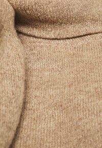 Beige neulekangas pehmeällä tekstuurilla, sileällä pinnalla ja hienovaraisilla sävyeroilla, jotka luovat tunnelmallisen ilmeen.