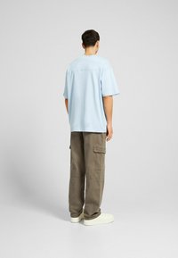 Světle modré oversized tričko s krátkým rukávem, spárované s olivovými cargo kalhotami s mnoha kapsami a bílými teniskami.