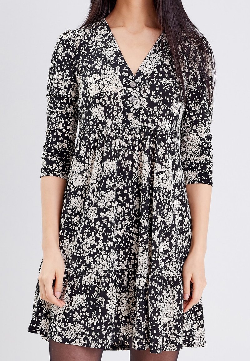 Robe noire à fleurs avec décolleté en V, manches trois-quarts et ourlet à volants ornée d'un motif de fleurs crème clair.