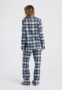Navy and white plaid flannel pajamas with a button-up top and loose-fitting pants. Soft texture, long sleeves, elastic waistband.