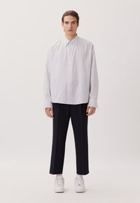 Camicia a righe bianca e viola chiaro, taglio oversize, abbinata a pantaloni scuri e sneakers bianche. Design minimalista, texture liscia.