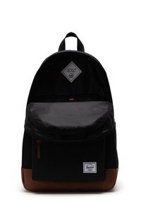 Zaino nero con un esterno testurizzato, fondo marrone e una fodera interna a righe. Presenta una maniglia superiore e un patch rettangolare con il logo del brand.