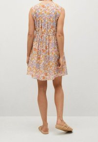 Robe florale avec un motif rose et jaune, corsage ajusté et jupe évasée. Dispose de manches courtes et d'une ceinture, assortie à des sandales beige.