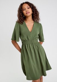 Robe verte olive avec un décolleté en V, des manches courtes, une taille élastique et une jupe évasée. Fabriquée dans un tissu léger et texturé.