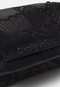 Czarna skórzana torebka z fakturowanymi kwiatowymi i paskowanymi wzorami, z wyraźnie wytłoczonym logo "Desigual" na skórzanej metce.