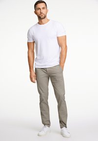 Witte crew-neck t-shirt, lichtgrijze gemusterde broek en witte sneakers. Het geheel heeft een casual, slimfit stijl met een soepele textuur.