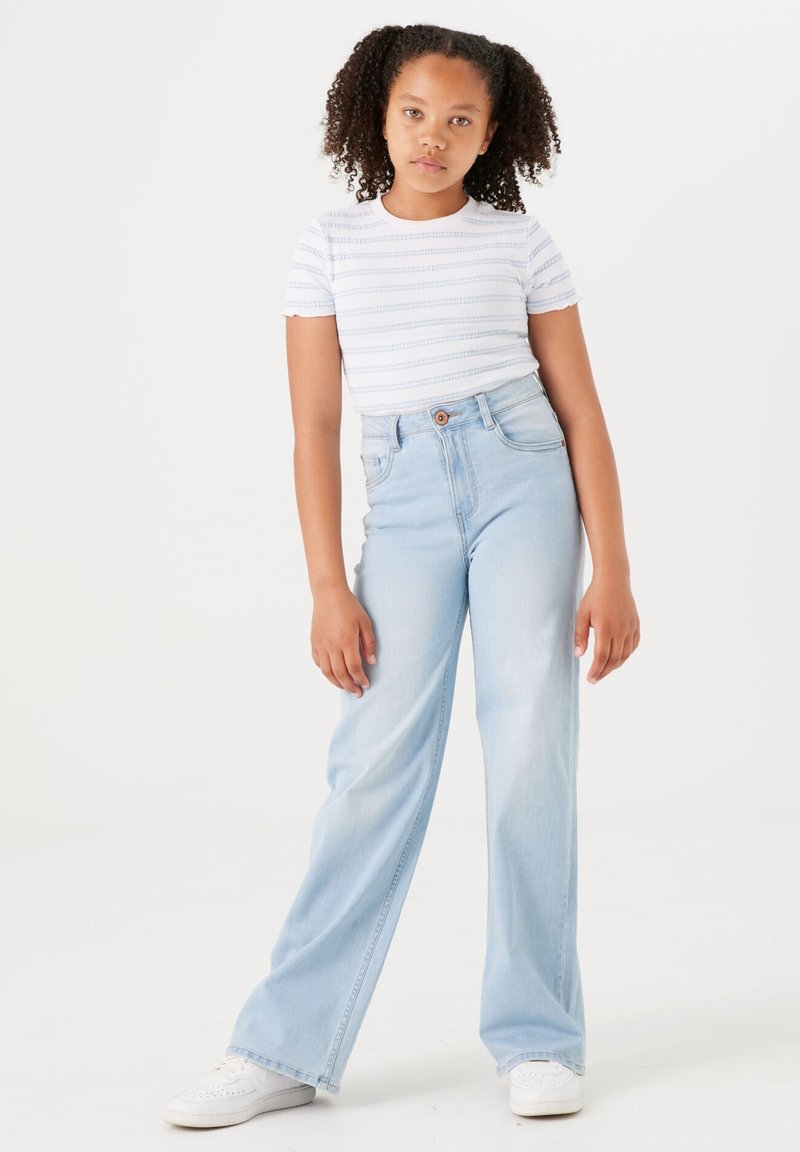 Hellblaue weite Jeans aus Denim mit hoher Taille und Knopfverschluss. Getragen mit einem kurzärmeligen, weiß gestreiften T-Shirt.