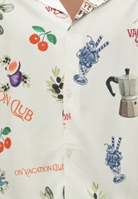 Πουκάμισο με τυπωμένα σχέδια κερασιών, σύκων, ελιών, ποτηριών με παγωτό, καφετιέρας και το κείμενο «ON VACATION CLUB» σε λευκό φόντο.