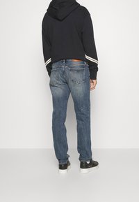 Denim jeans with a faded blue color, featuring a straight fit, subtle distressing, and a brown leather patch on the back waistband.