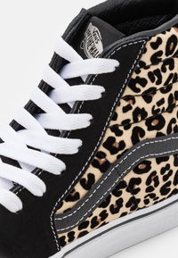 Hochschnittige Vans-Sneaker mit weißen Schnürsenkeln, schwarzem Wildleder, Seiten aus Leopardenmusterstoff und dem charakteristischen weißen gestickten Streifen.