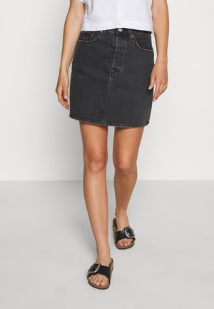 Sort denim nederdel med en tætsiddende form, frontlommer og diskrete syninger. Kombineret med sorte slidesandaler.